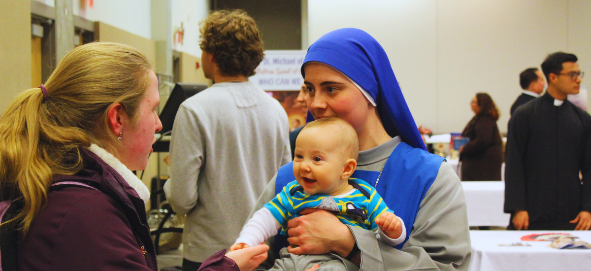 A student with a sister holding a baby at a vocations fair